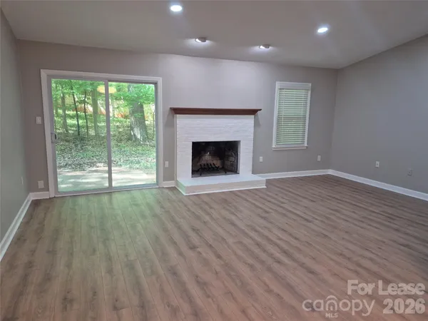 an empty room with wooden floor fireplace and windows