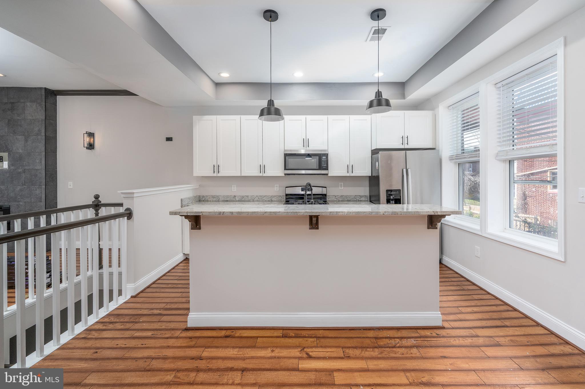 3506 Reisterstown Road Baltimore, MD 21215 - Photo 9 of 32 a large kitchen with stainless steel appliances granite countertop a stove a refrigerator a sink and white cabinets with wooden floor
