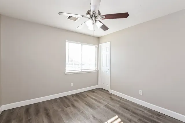 an empty room with wooden floor fan and windows