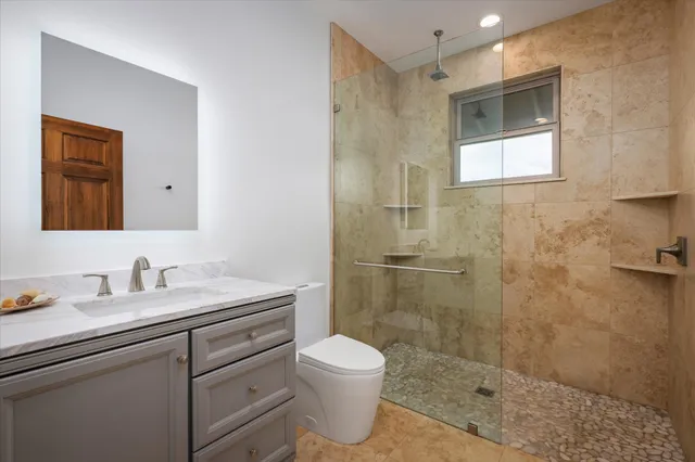 a bathroom with a toilet sink vanity granite and shower
