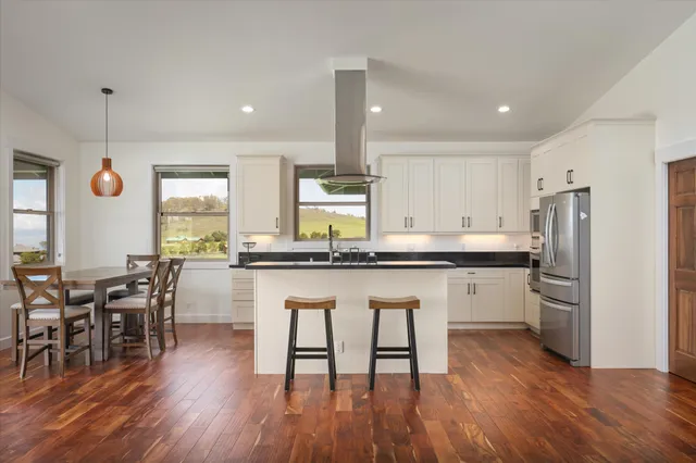 a kitchen with stainless steel appliances granite countertop a table chairs stove a sink and white cabinets