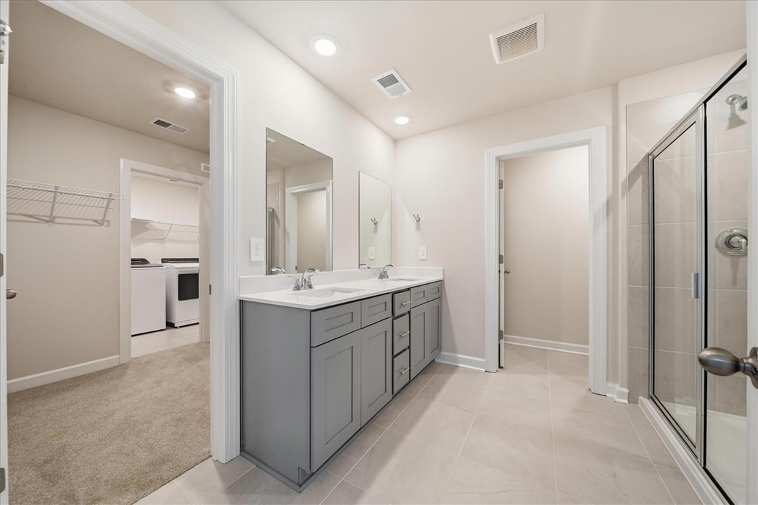 102 Gibbon Way Gray Court, SC 29645 - Photo 19 of 49 This primary bathroom features dual vanities, a spacious walk-in shower, and an adjacent laundry area.
