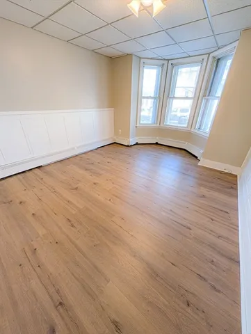 an empty room with wooden floor and windows with curtains