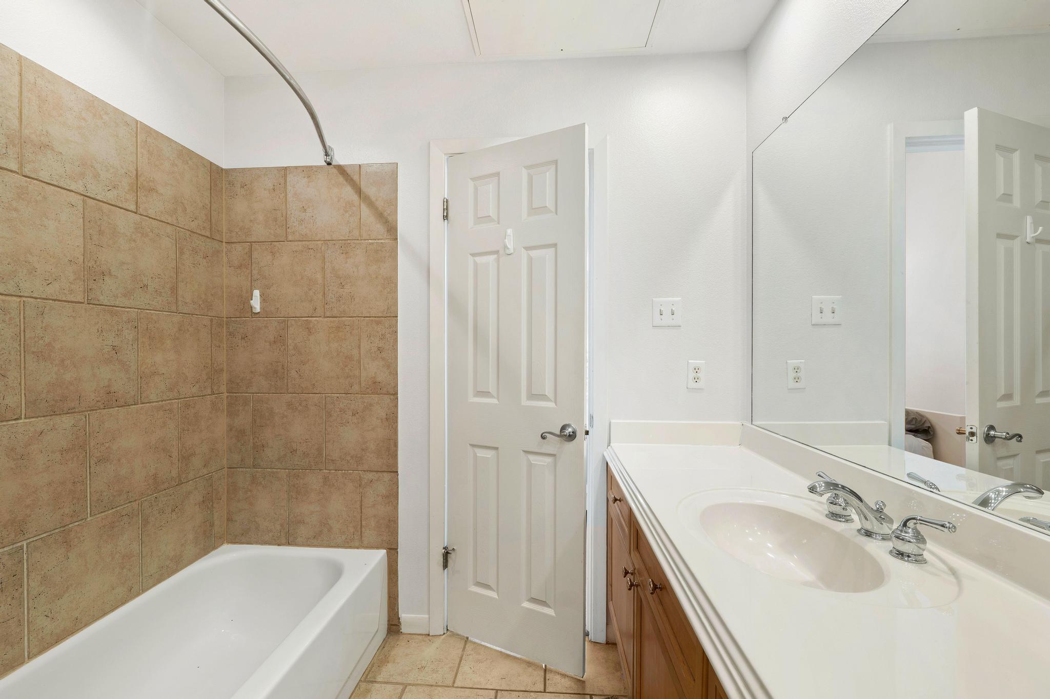 2918 Ranch Road 620, Unit J162 Austin, TX 78734 - Photo 24 of 26 Bathroom featuring a combination bathtub and shower with neutral-toned tile surround, a single vanity with an integrated sink, a white countertop, and a large wall-mounted mirror