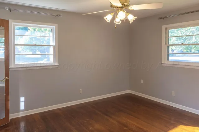 an empty room with wooden floor windows and fan