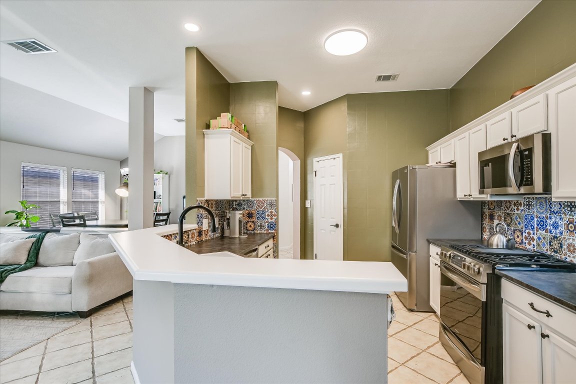 1302 Redbud Lane Leander, TX 78641 - Photo 10 of 28 a kitchen with stainless steel appliances a sink dishwasher a refrigerator a stove top oven a dining table and chairs with wooden floor