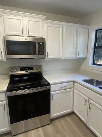 a view of a refrigerator in kitchen and an empty room with wooden floor