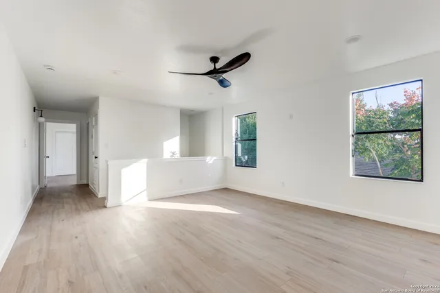 an empty room with wooden floor a ceiling fan and windows