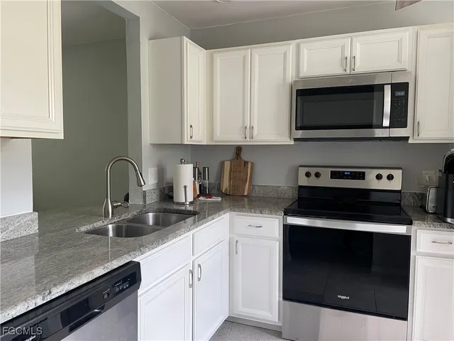 a kitchen with stainless steel appliances granite countertop a sink dishwasher a stove and a microwave oven with white cabinets