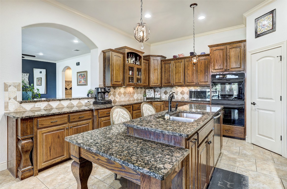 Undisclosed Address Georgetown, TX 78633 - Photo 16 of 38 Kitchen with brown cabinets, glass insert cabinets, backsplash, dark stone countertops, and crown molding