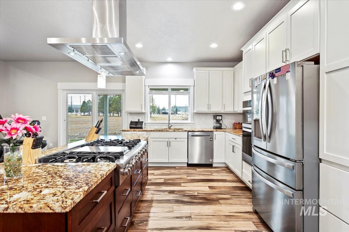 17322 Can-Ada Road Nampa, ID 83687 - Photo 11 of 44 Kitchen featuring white cabinetry, light stone countertops, stainless steel appliances, recessed lighting, and island range hood