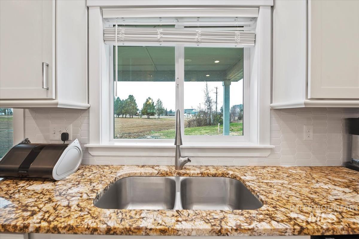 17322 Can-Ada Road Nampa, ID 83687 - Photo 12 of 44 Kitchen view of decorative backsplash, light stone countertops, and white cabinetry