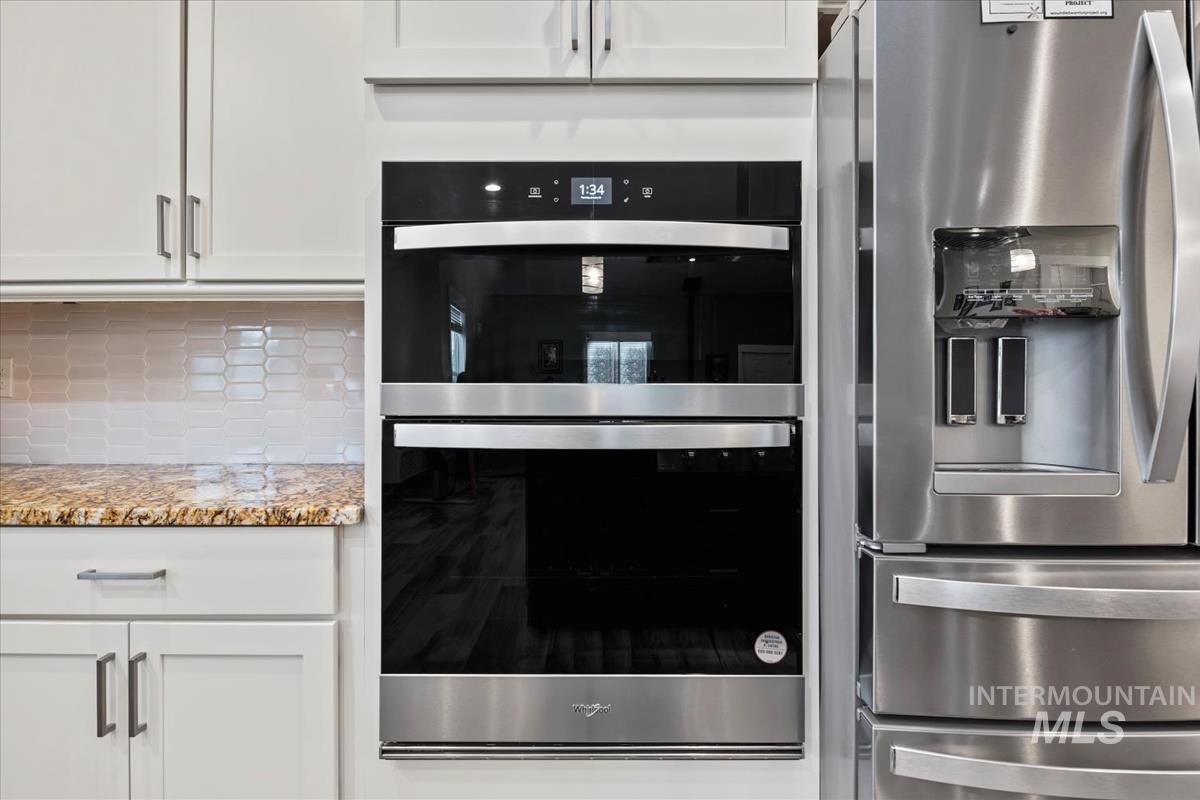 17322 Can-Ada Road Nampa, ID 83687 - Photo 4 of 44 Kitchen with appliances with stainless steel finishes, white cabinetry, light stone countertops, and tasteful backsplash