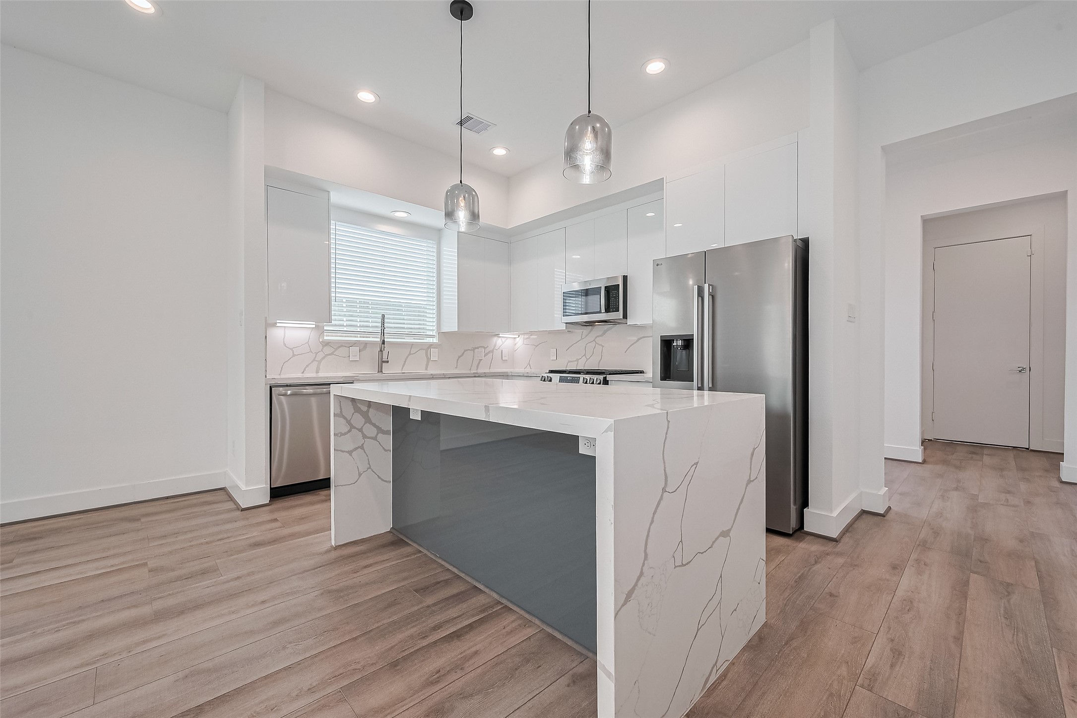 3510 Hadley Street Houston, TX 77004 - Photo 1 of 48 A modern kitchen that blends clean design with everyday functionality—featuring a striking waterfall-edge quartz island, sleek white cabinetry, bar seating, and layered lighting that adds warmth and sophistication.