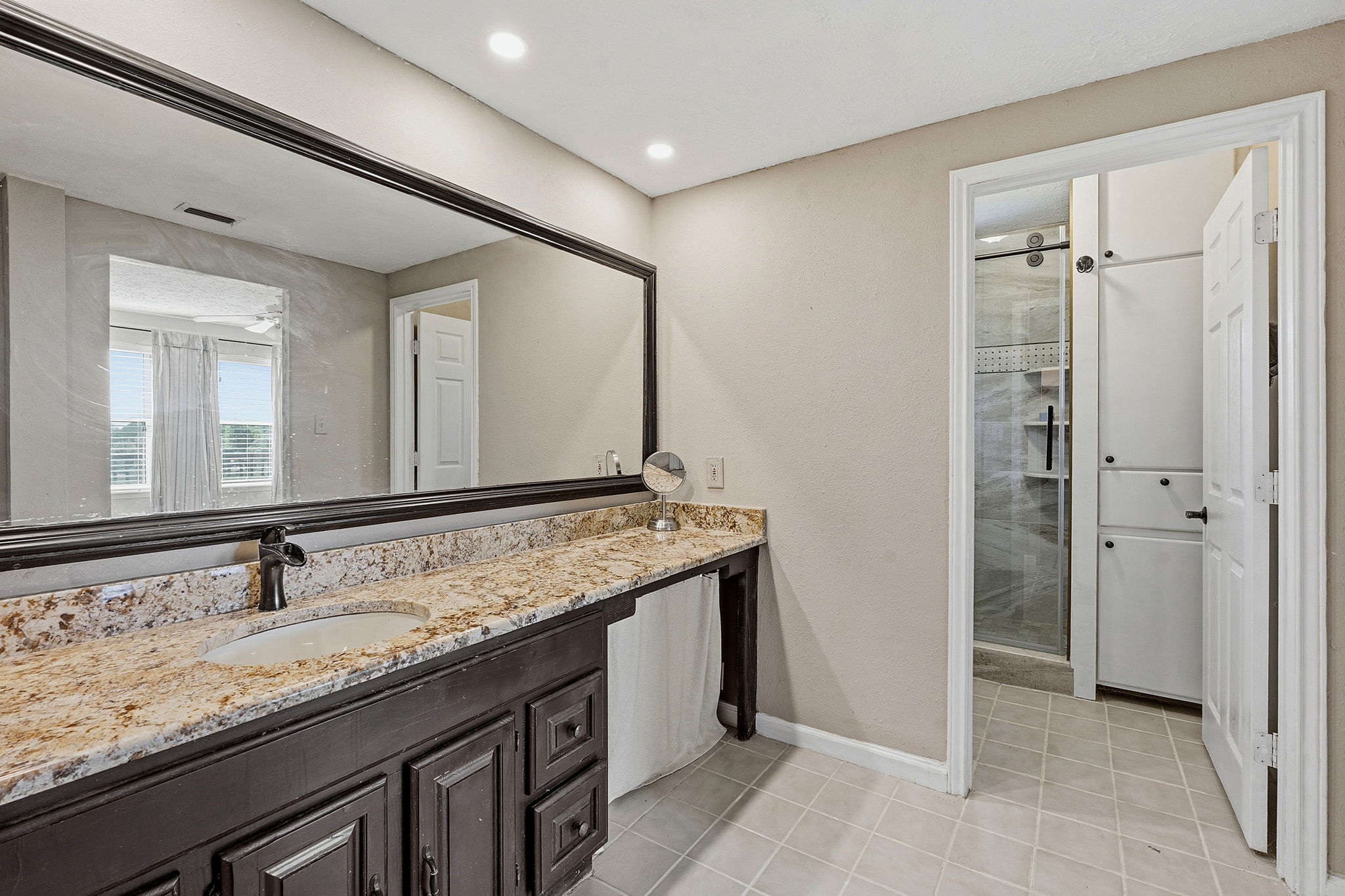 3230 West Fitzhugh Road Dripping Springs, TX 78620 - Photo 19 of 34 Granite counters and dark cabinetry define this spacious primary bathroom vanity, leading to a shower and built-in storage.