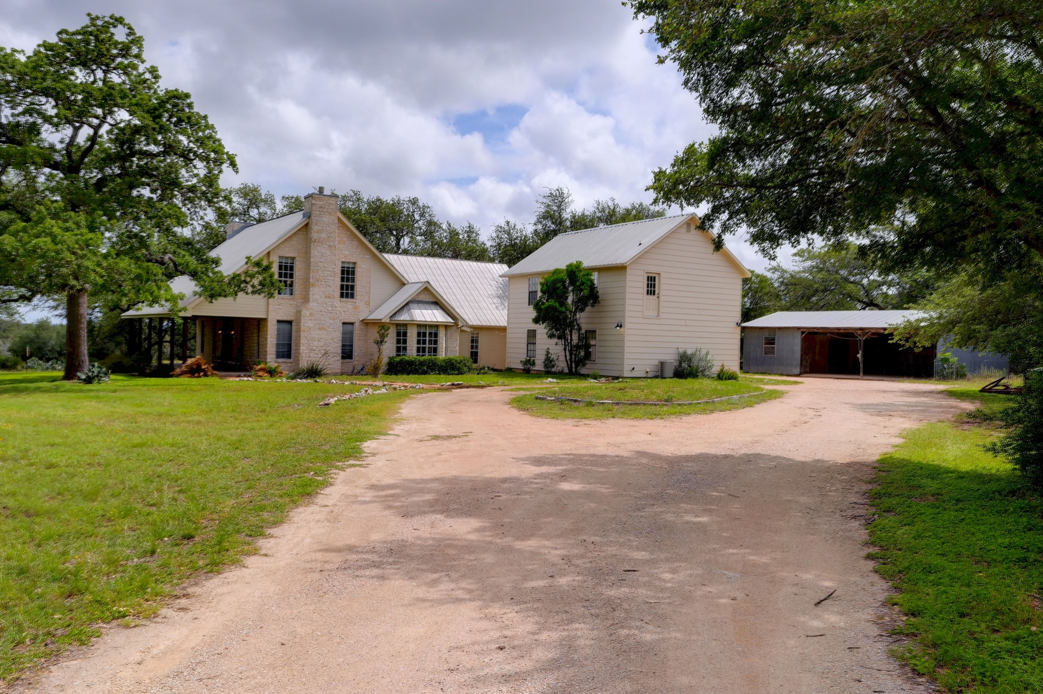 364 Nameless Road Driftwood, TX 78619 - Photo 3 of 32 A spacious circular gravel drive leads to a charming residence with a covered porch and an adjacent three car detached garage with a full garage apartment upstairs.