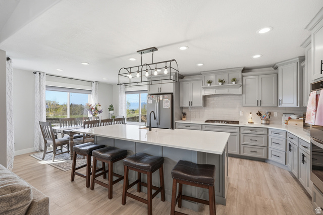638 Canyon Rim Road Smithfield, UT 84335 - Photo 9 of 56 Kitchen with gray cabinetry, a breakfast bar, an island with sink, stainless steel appliances, and light wood-style floors