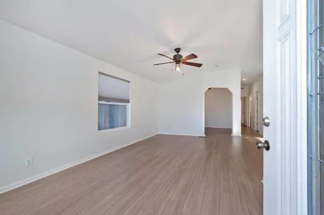an empty room with wooden floor chandelier fan and windows