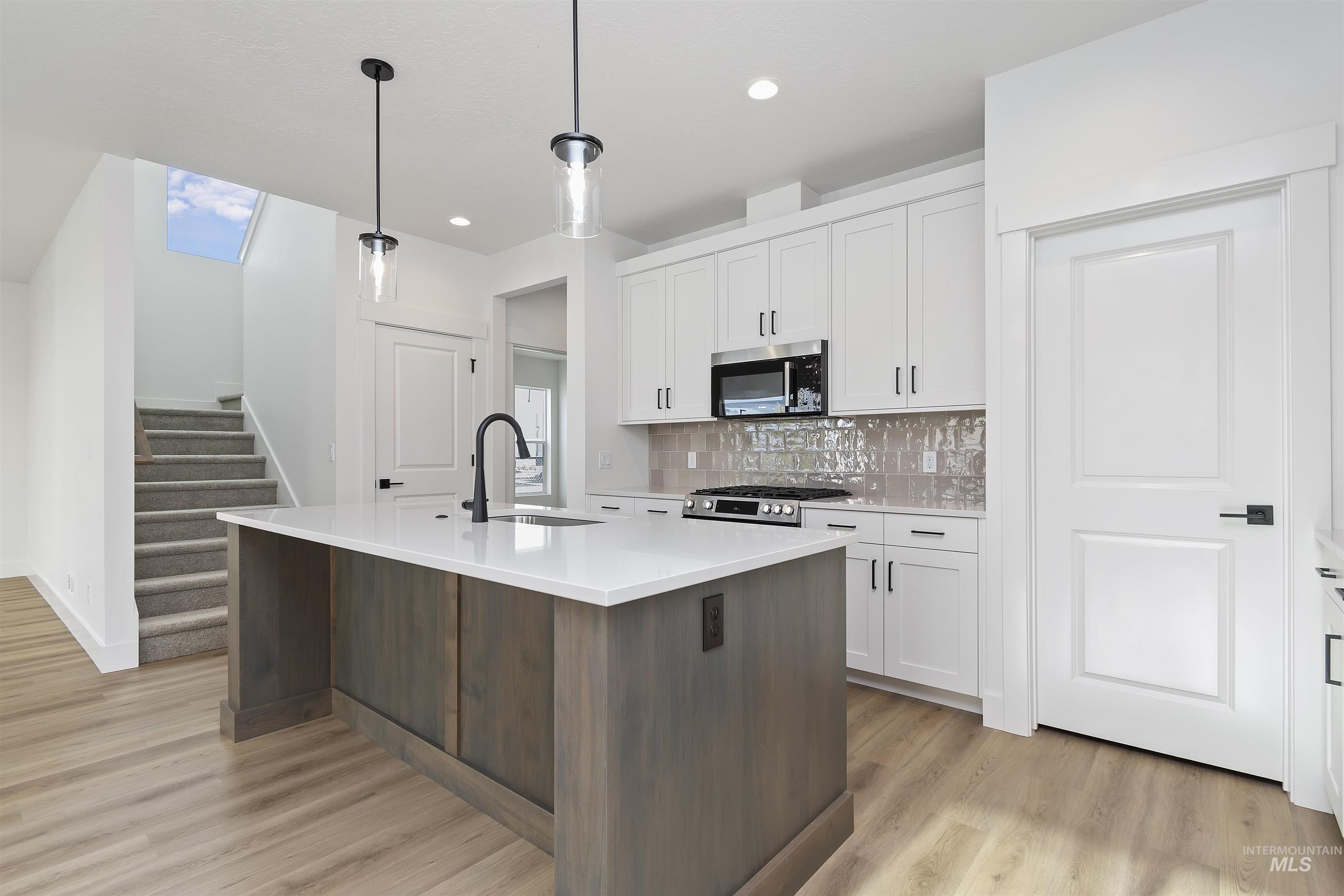 764 South Calhoun Lane Star, ID 83669 - Photo 8 of 48 Kitchen featuring white cabinets, a kitchen island with sink, appliances with stainless steel finishes, dark brown cabinetry, and hanging light fixtures