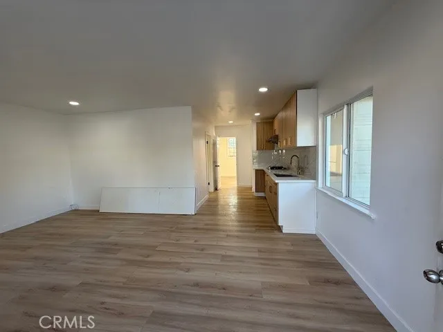 a view of an empty room with wooden floor and a kitchen
