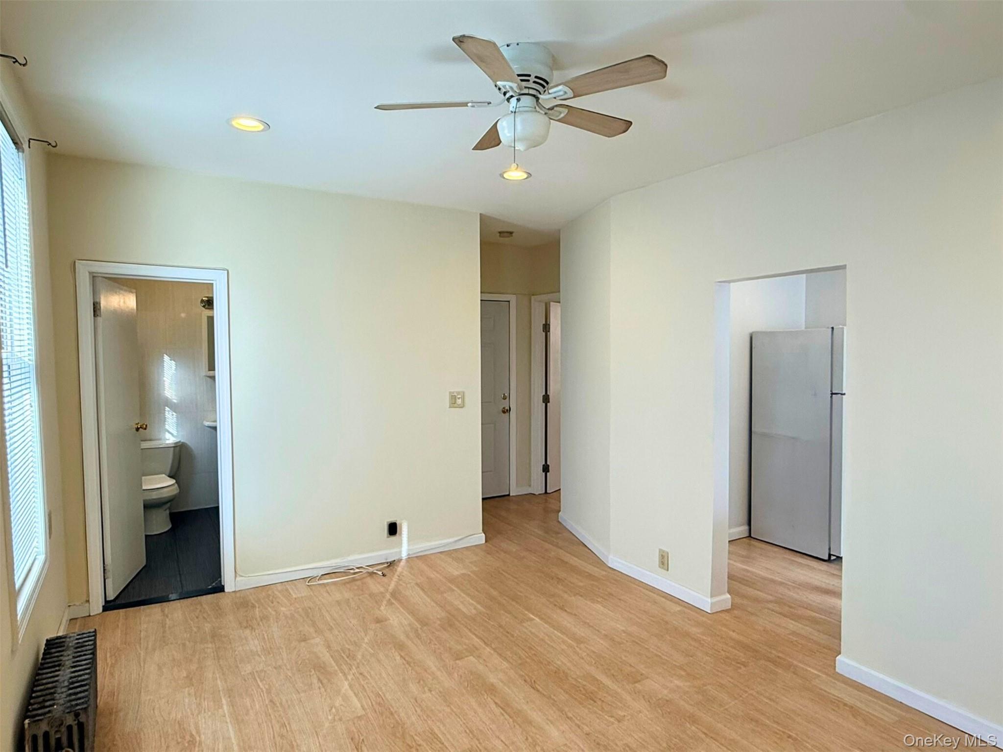52-05 35th Street, Unit 2 Queens, NY 11101 - Photo 5 of 32 Unfurnished bedroom featuring freestanding refrigerator, radiator, light wood-style floors, ceiling fan, and connected bathroom