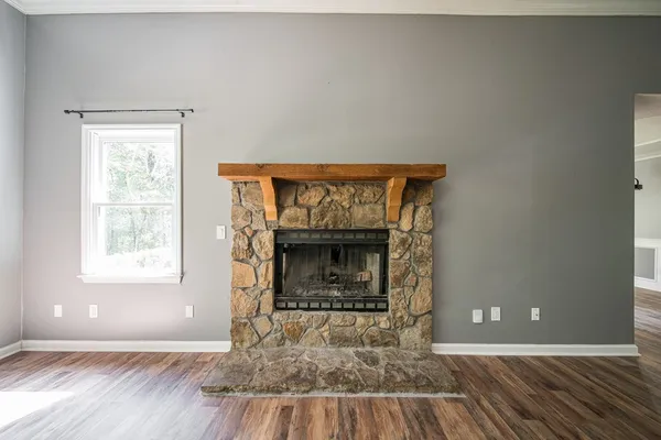 a view of an empty room with wooden floor fireplace and a window