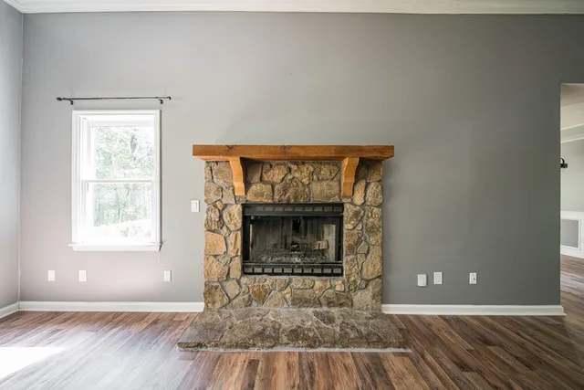a view of an empty room with wooden floor fireplace and a window