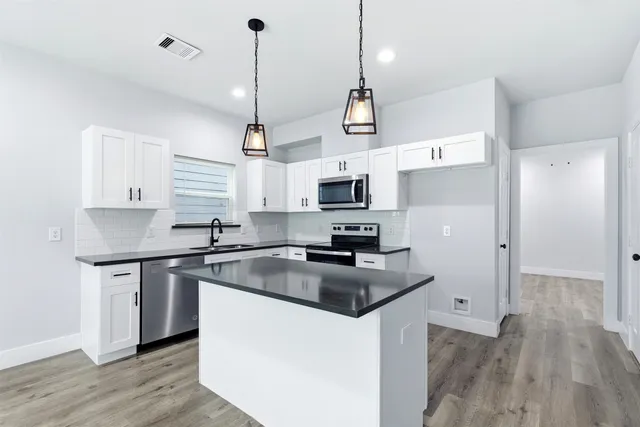 a kitchen with stainless steel appliances granite countertop a sink a stove a refrigerator and island with wooden floor