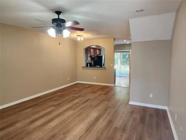 an empty room with wooden floor chandelier fan and windows