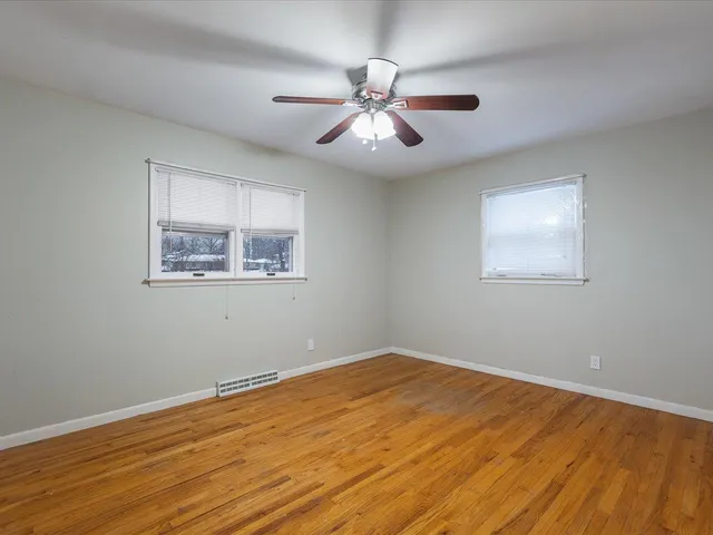 a view of an empty room with wooden floor and a ceiling fan