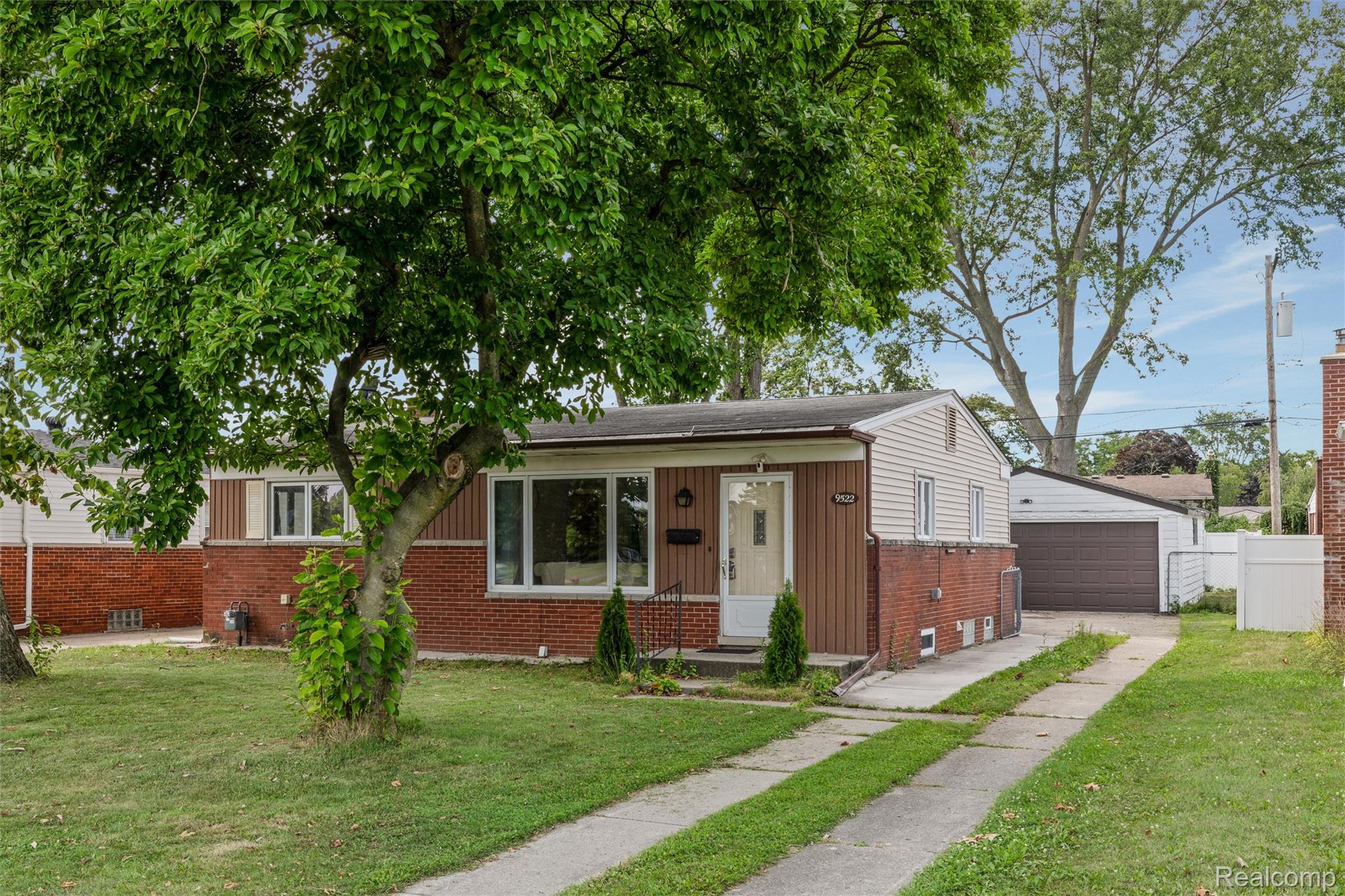 9522 Pardee Road Taylor, MI 48180 - Photo 2 of 25 Brick and siding exterior, front yard with mature tree, concrete driveway, detached garage with dark overhead door, and white privacy fencing