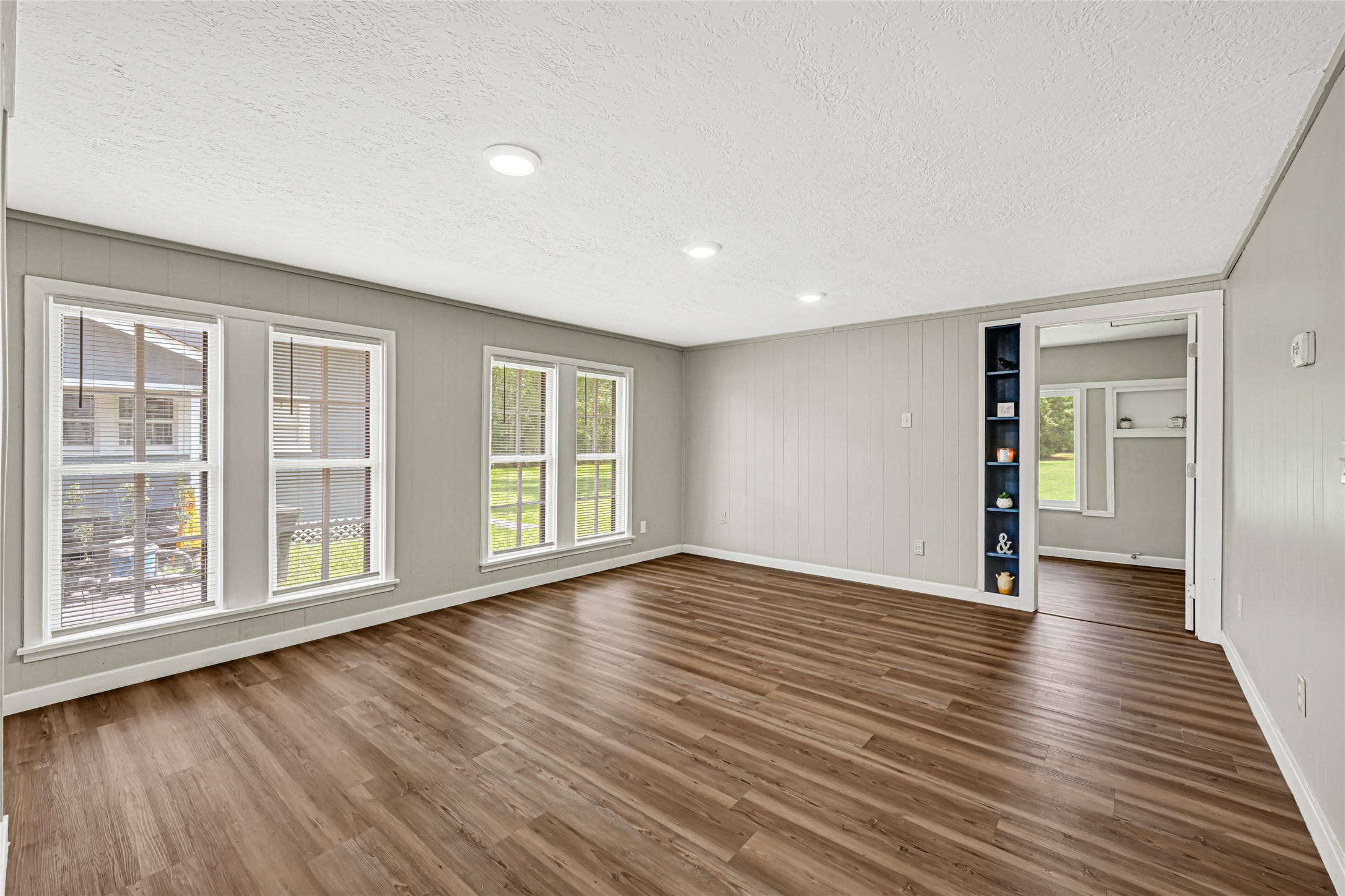 4568 Dunnam Road, Unit B Houston, TX 77345 - Photo 7 of 15 Bright and spacious living area featuring large windows, wood laminate flooring, and built-in shelving, perfect for a cozy and inviting atmosphere. View taken from the kitchen/dining.