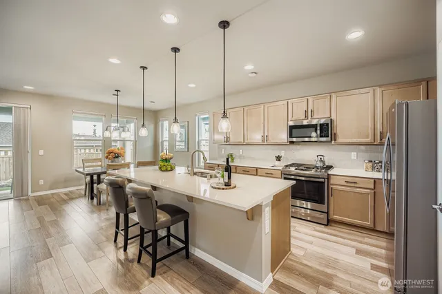 a kitchen with stainless steel appliances granite countertop a stove a sink a refrigerator a stove a dining table and chairs with wooden floor