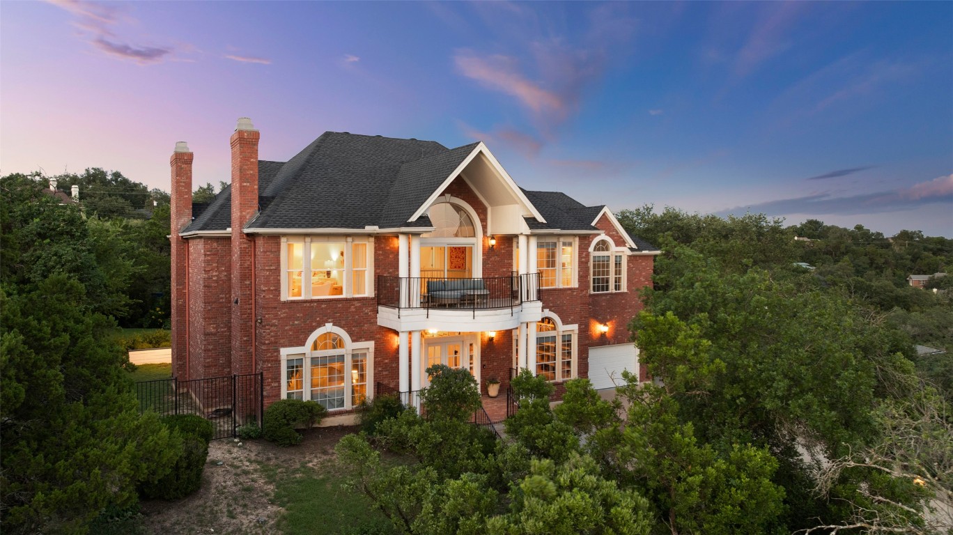 Georgian-style home featuring a balcony, brick siding, a chimney, and a shingled roof