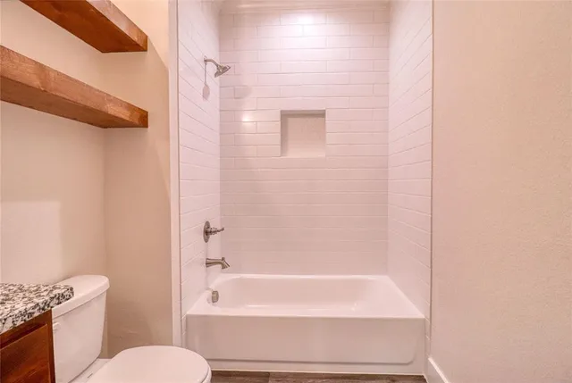 a bathroom with a granite countertop bathtub shower sink mirror and toilet