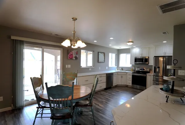 a kitchen with stainless steel appliances granite countertop a refrigerator a stove top oven a sink dishwasher a dining table and chairs with wooden floor