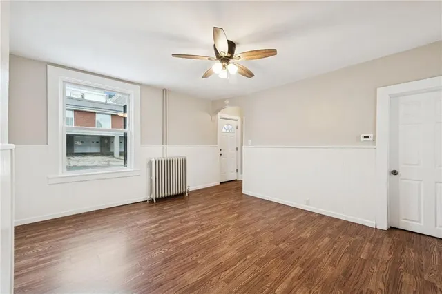 an empty room with wooden floor chandelier fan and windows