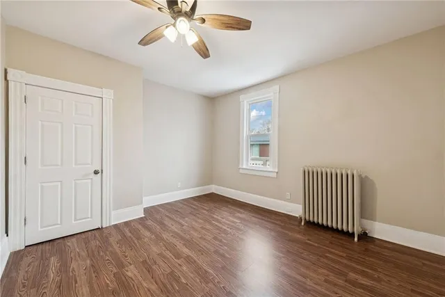 an empty room with wooden floor chandelier fan and windows