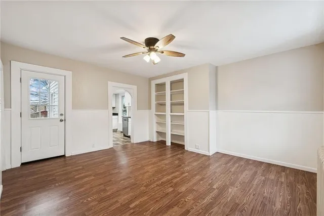 an empty room with wooden floor chandelier fan and windows