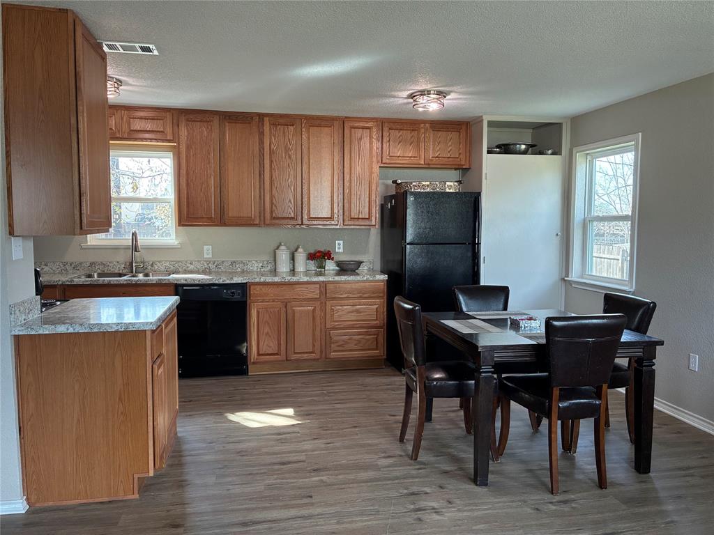 5066 East Highway 199 Springtown, TX 76082 - Photo 6 of 15 Kitchen featuring wood finish cabinetry, light countertops, black appliances, healthy amount of natural light, and a textured ceiling