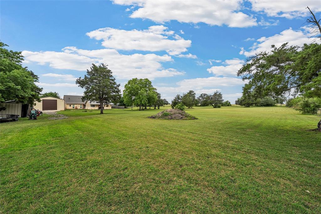 1117 Downsville Road Robinson, TX 76706 - Photo 32 of 40 Expansive green lawn with scattered mature trees and a distant single-story structure featuring a light-colored exterior and a dark roof