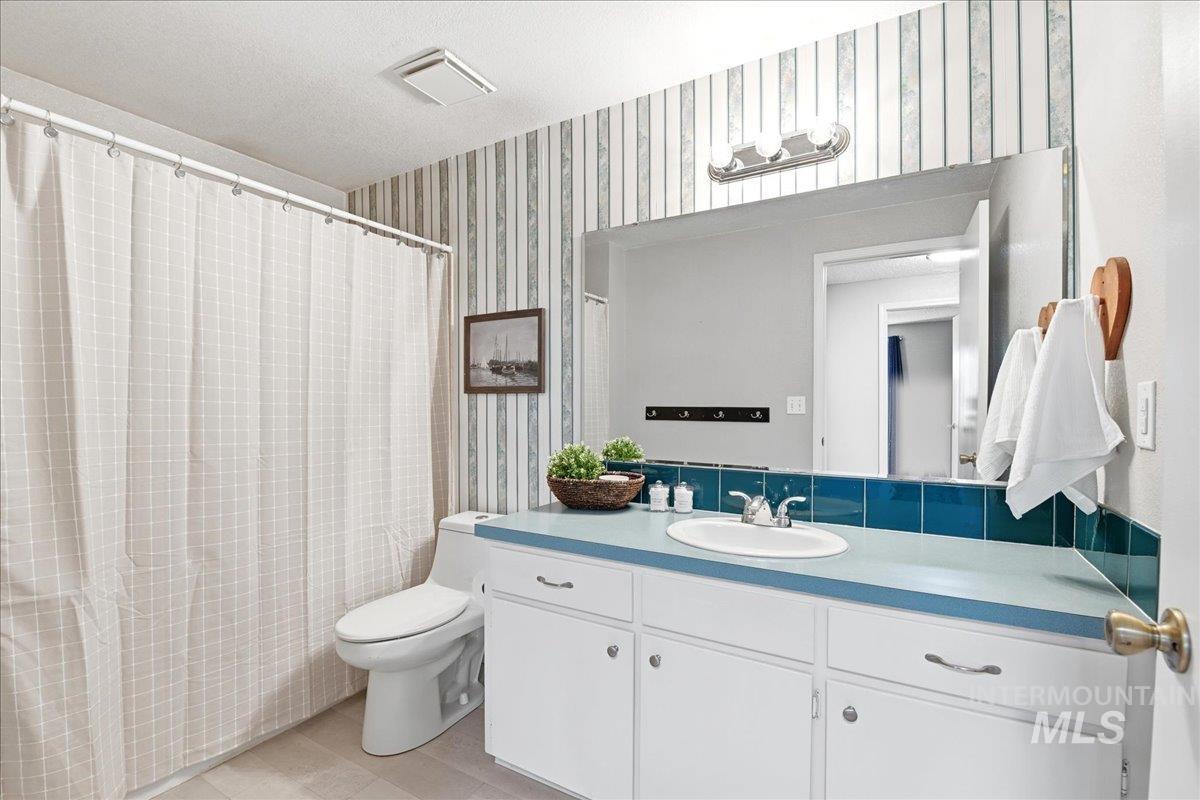 11842 Tioga Street Boise, ID 83709 - Photo 27 of 50 Bathroom featuring a light blue countertop, white cabinetry with silver-tone hardware, an undermount sink, a large wall-mounted mirror, and a tiled backsplash