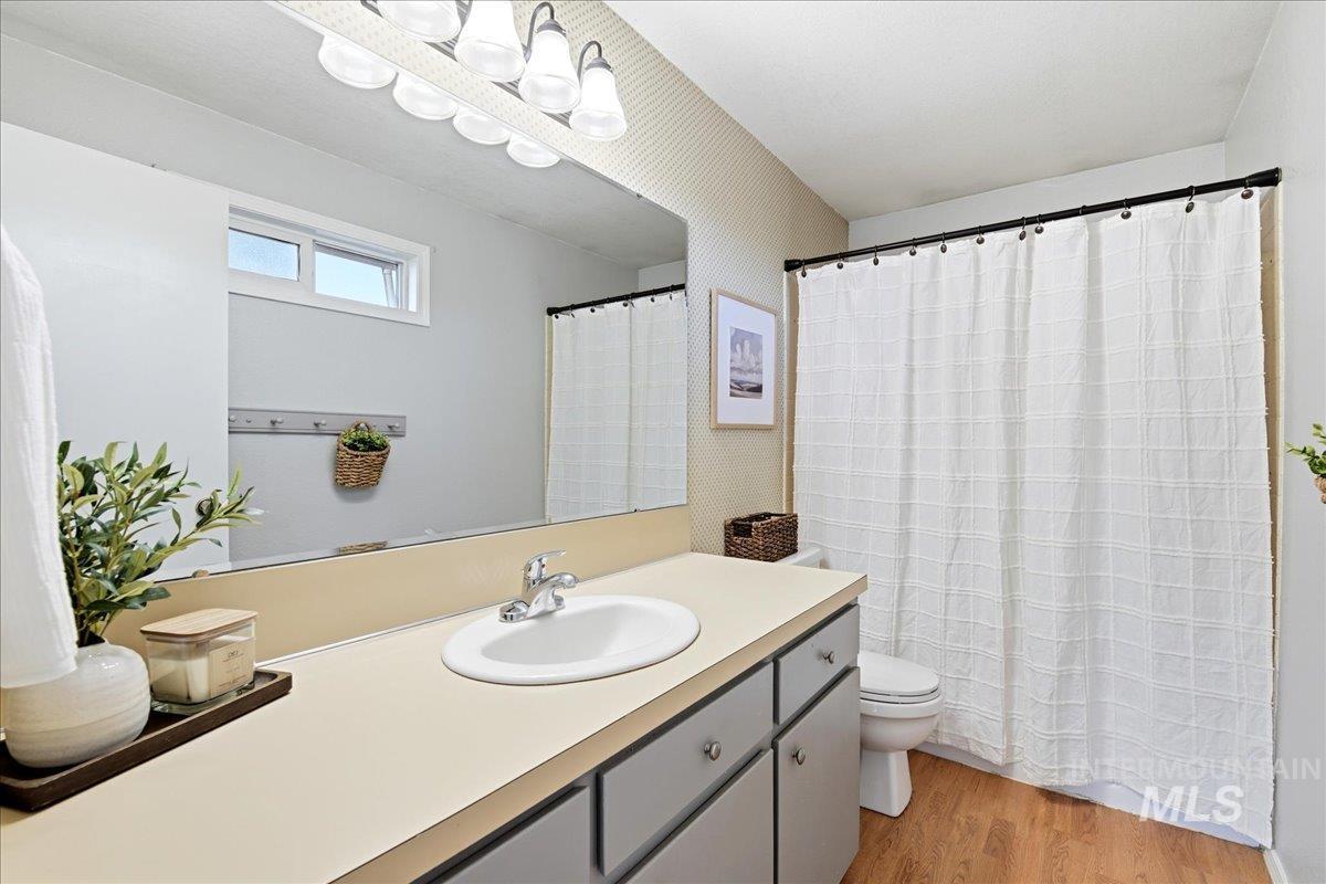 11842 Tioga Street Boise, ID 83709 - Photo 29 of 50 Bathroom featuring a vanity with an integrated sink, a rectangular mirror, a light fixture with multiple sconces, and wood-finish flooring