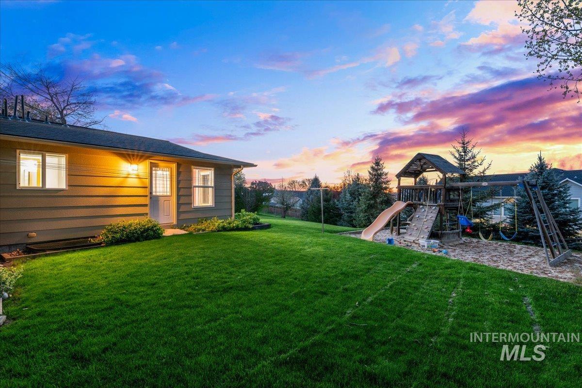 11842 Tioga Street Boise, ID 83709 - Photo 39 of 50 Expansive sloped lawn with a built-in play structure featuring a slide, climbing wall, and swing set over a sand base