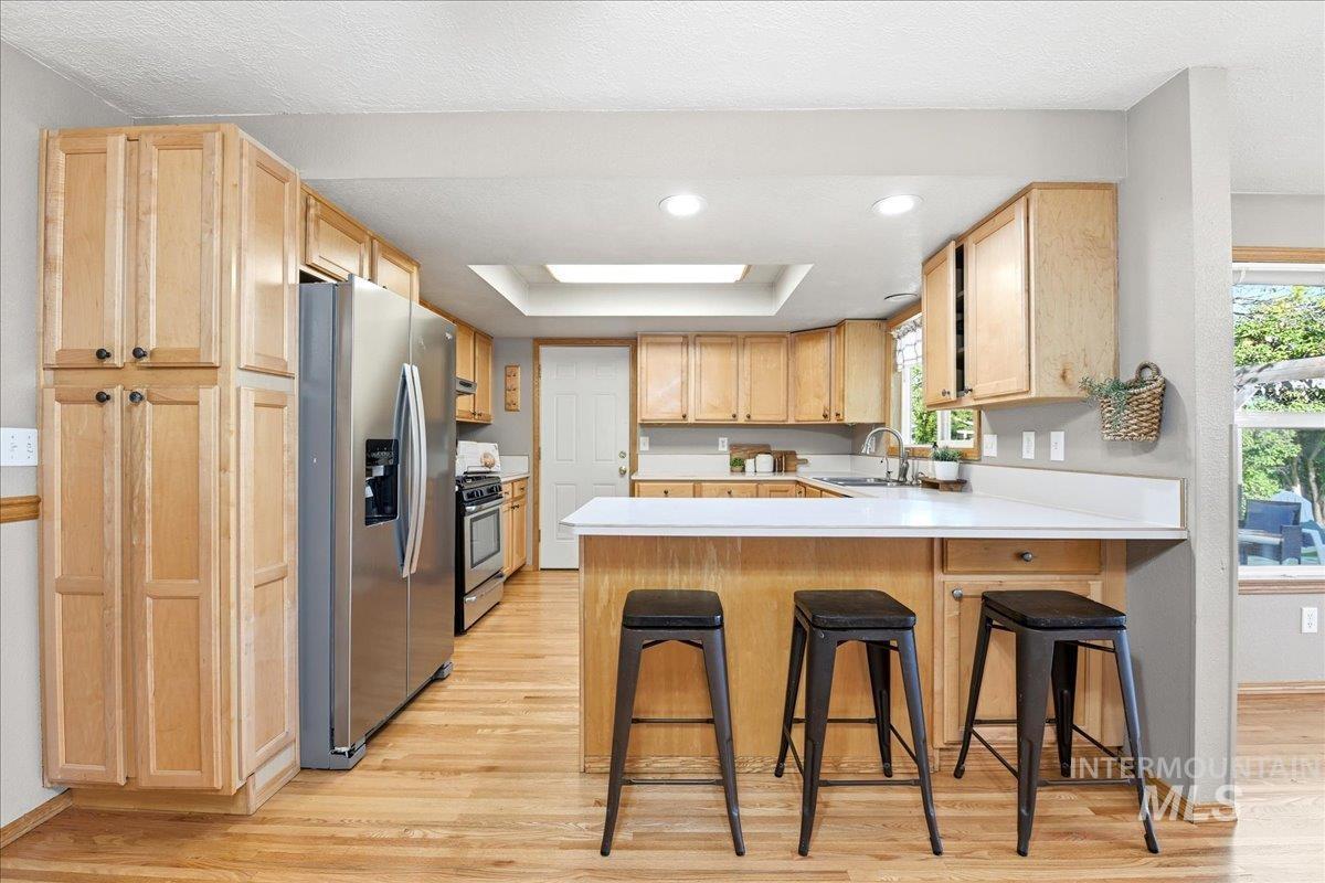 11842 Tioga Street Boise, ID 83709 - Photo 10 of 50 Kitchen featuring light wood cabinetry, stainless steel appliances, a white countertop island with seating, a skylight, and wood-finish flooring