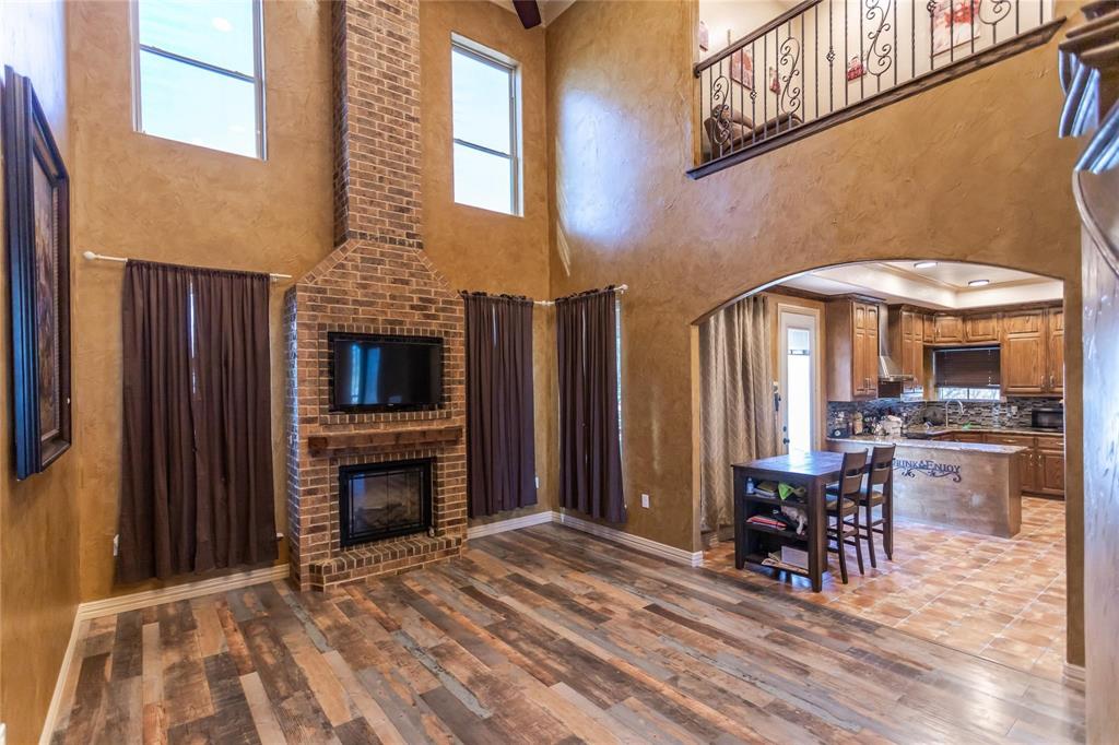 8900 Holly Road Alvarado, TX 76009 - Photo 6 of 17 Two-story brick fireplace, wood-finish flooring, arched entryway, open-concept kitchen, and second-story interior balcony with wrought iron railing