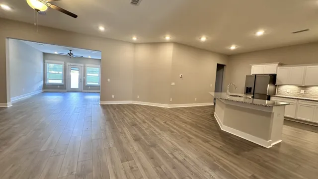 a view of an empty room with wooden floor and a ceiling fan
