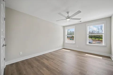 an empty room with wooden floor ceiling fan and windows