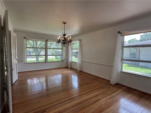 an empty room with wooden floor chandelier and windows