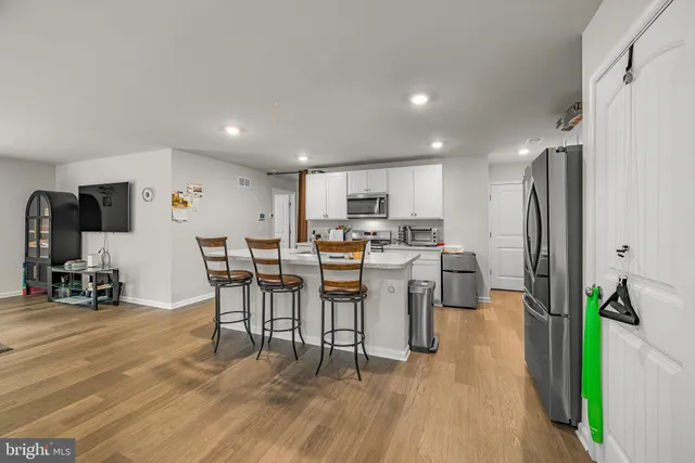 a open kitchen with stainless steel appliances kitchen island granite countertop a table chairs and a refrigerator